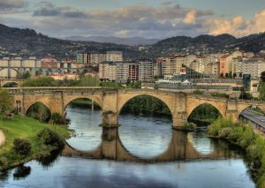 Foto de la ciudad de Ourense que se puede ver detrás del puente de piedra y que invita a visitar y pasear con tu perro